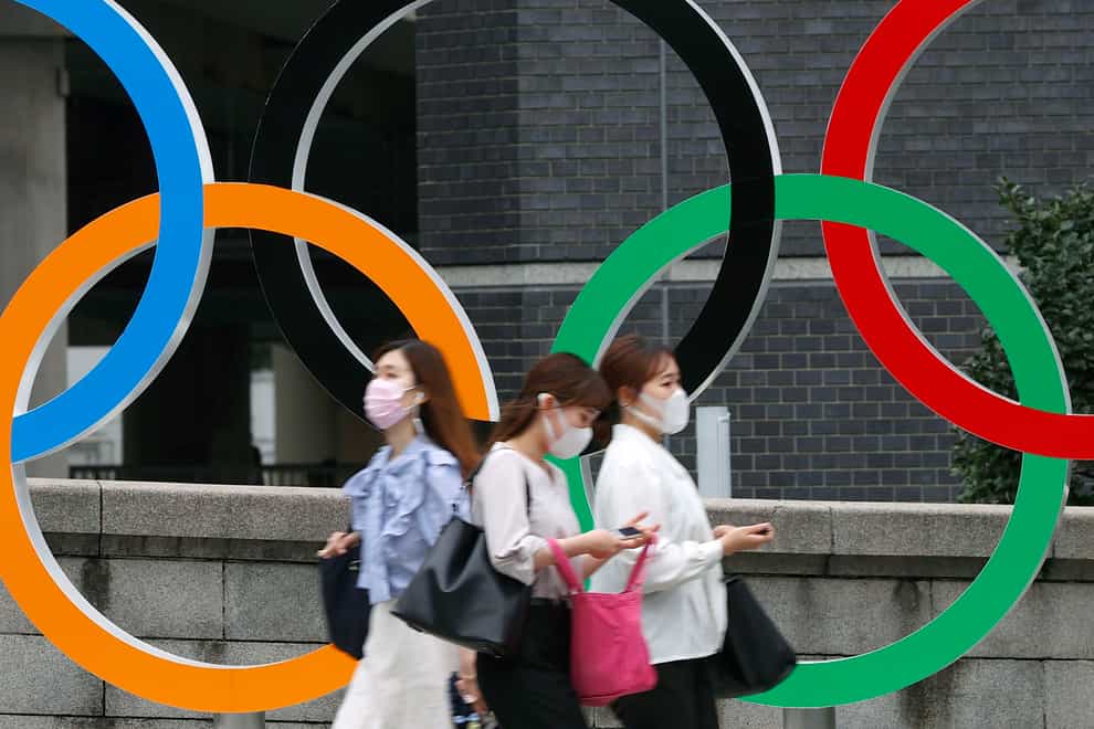 People wearing face masks walk past the Olympics Rings statue in Tokyo