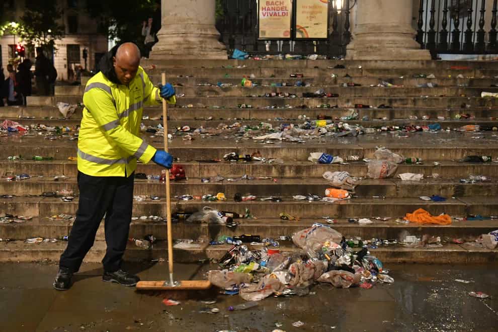 A street cleaner clears up litter strewn on the ground in front of St Martin-In-The-Fields church, in Trafalgar Square
