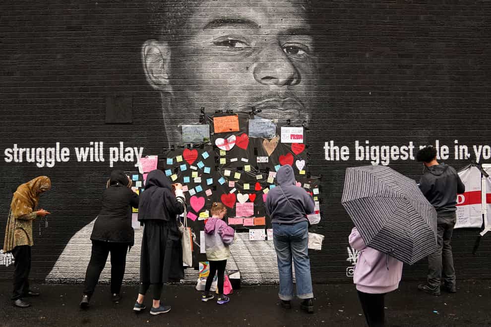 <p>People place messages of support on top of bin liners that were taped over offensive wording on the mural of Manchester United striker and England player Marcus Rashford in Withington</p>