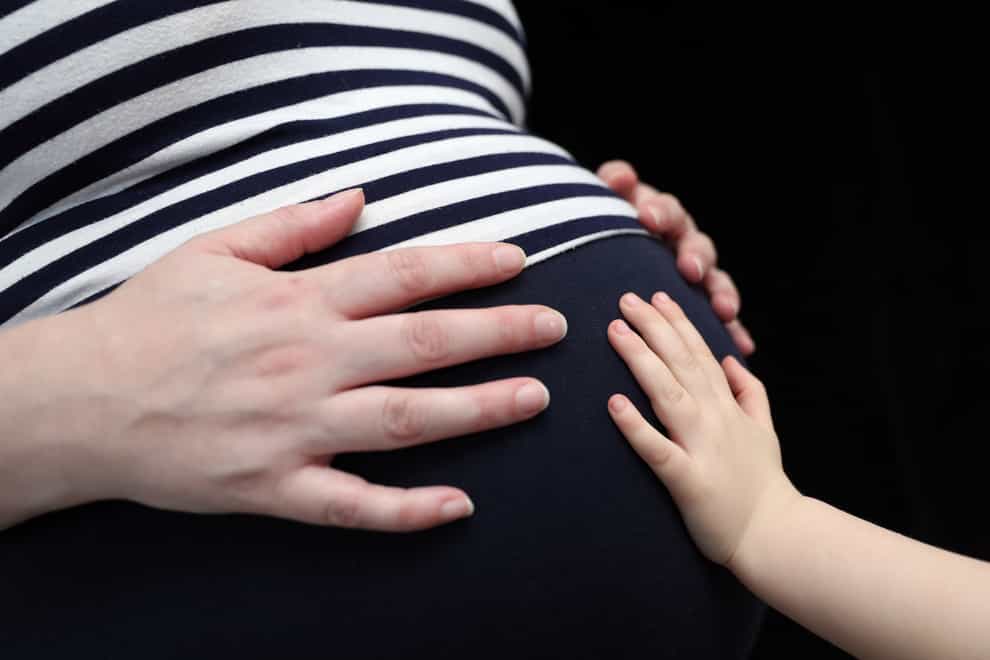A child places a hand on the stomach of a pregnant woman