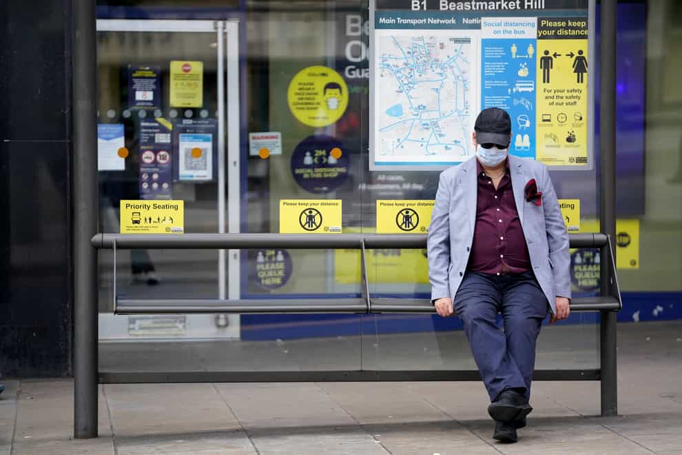 A member of the public wearing a mask sits at a bus stop in Nottingham (Zac Goodwin/PA)