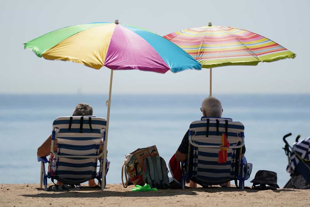 People sit under umbrallas as they enjoy the hot weather at Bournemouth beach (Andrew Matthews/PA)