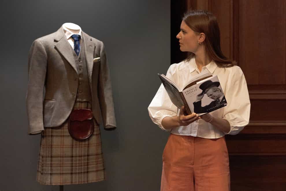 A member of staff looking at the late Duke of Edinburgh’s kilt, which forms part of the display (David Cheskin/Royal Collection Trust/PA)