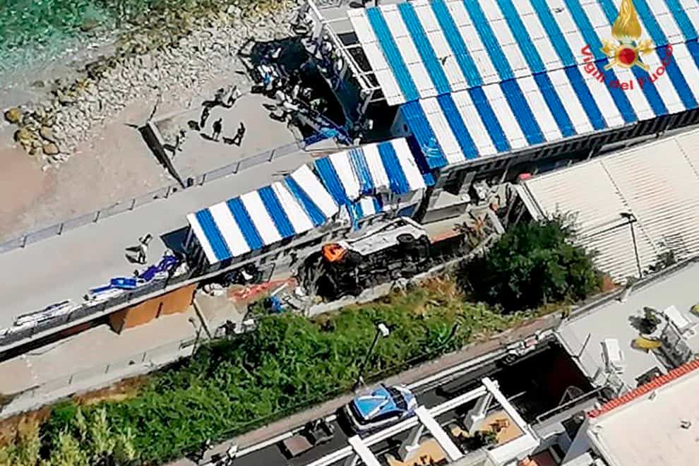 A bus lies on its side after crashing through a guardrail, on the island of Capri, Italy, Thursday, July 22, 2021. A public bus on the Italian vacation island of Capri crashed through a guardrail and landed on a beach resort area Thursday, fatally injuring the driver, firefighters and Capri’s mayor said (Italian Firefighters via AP)