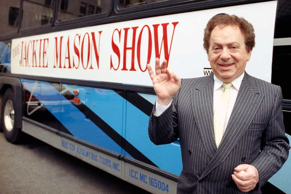 Comedian Jackie Mason stands beside a bus displaying a sign advertising his TV show in 1992 (AP)