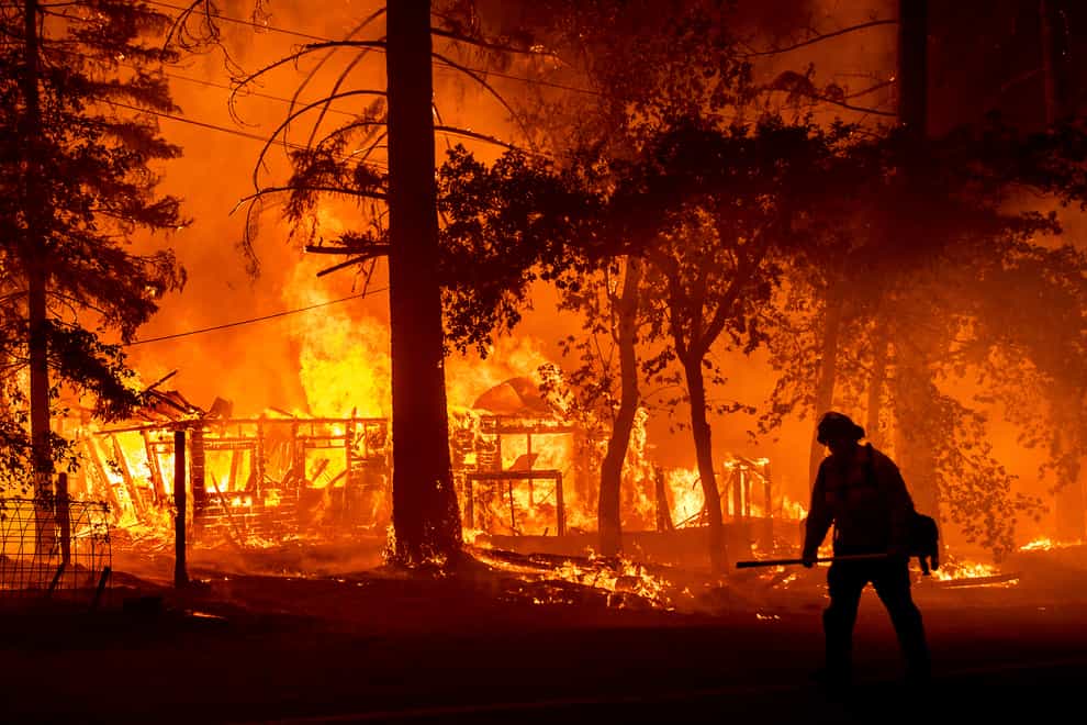 A firefighter passes a burning home as the Dixie Fire flares in Plumas County (AP)