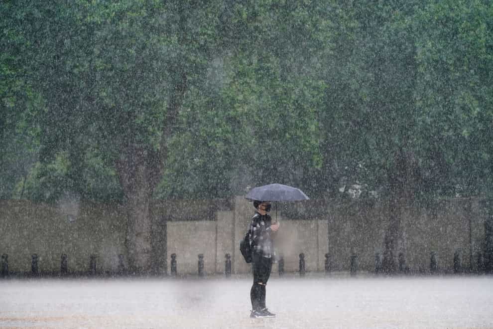 A woman stands in the rain in Horse Guards Parade, Westminster as heavy rain sweeps through central London. Thunderstorms bringing lightning and torrential rain to the south are set to continue until Monday, forecasters have said. Picture date: Sunday July 25, 2021.