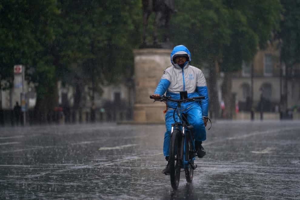A man rides a bike along Whitehall as heavy rain sweeps through central London (Victoria Jones/PA)