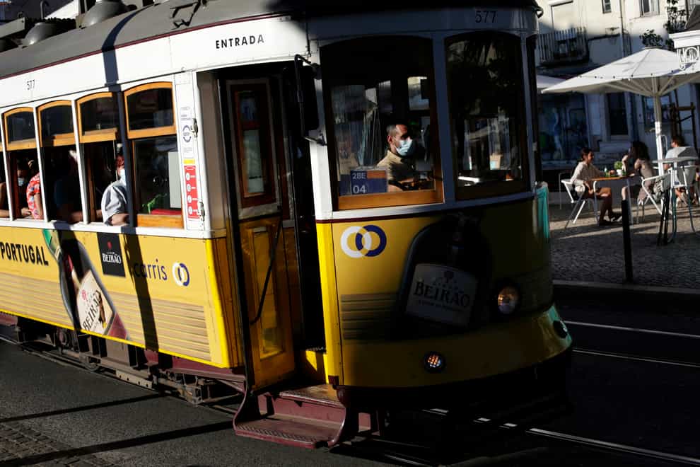 A tram conductor wearing a face mask drives through Lisbon’s Graca neighbourhood (Armando Franca/AP)
