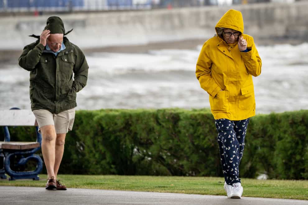 People pull down their hoods to shelter from the wind as they walk along the sea front in Porthcawl, Wales (Ben Birchall/PA).