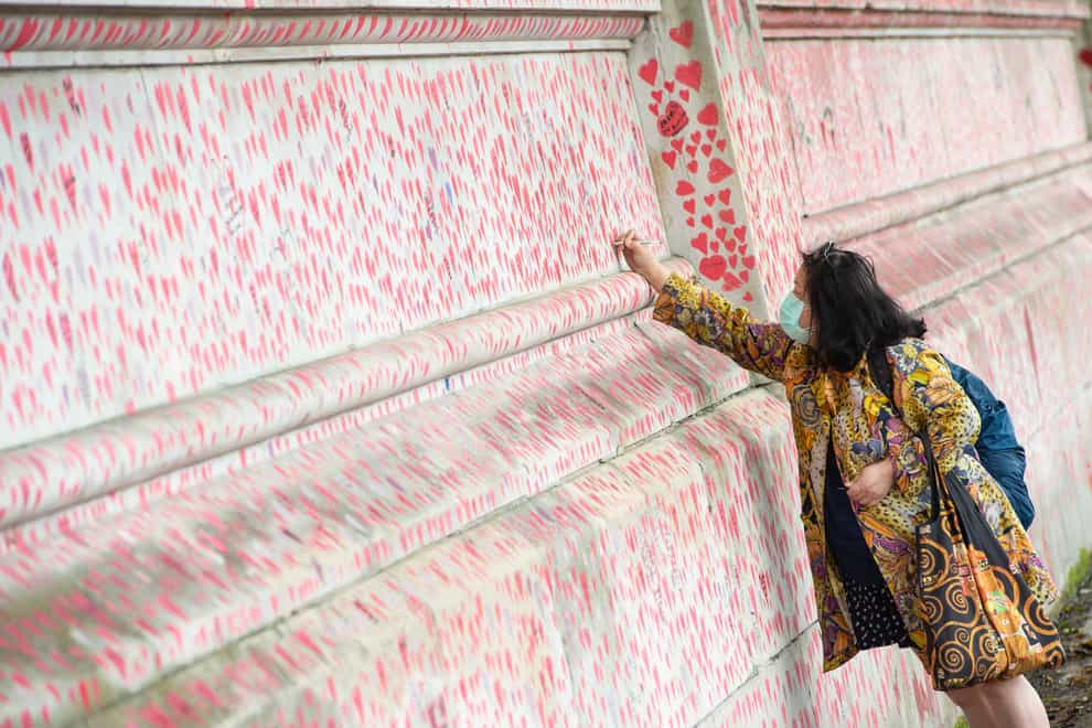 A woman writes a message on the Covid memorial wall in Westminster, London (Dominic Lipinski/PA)