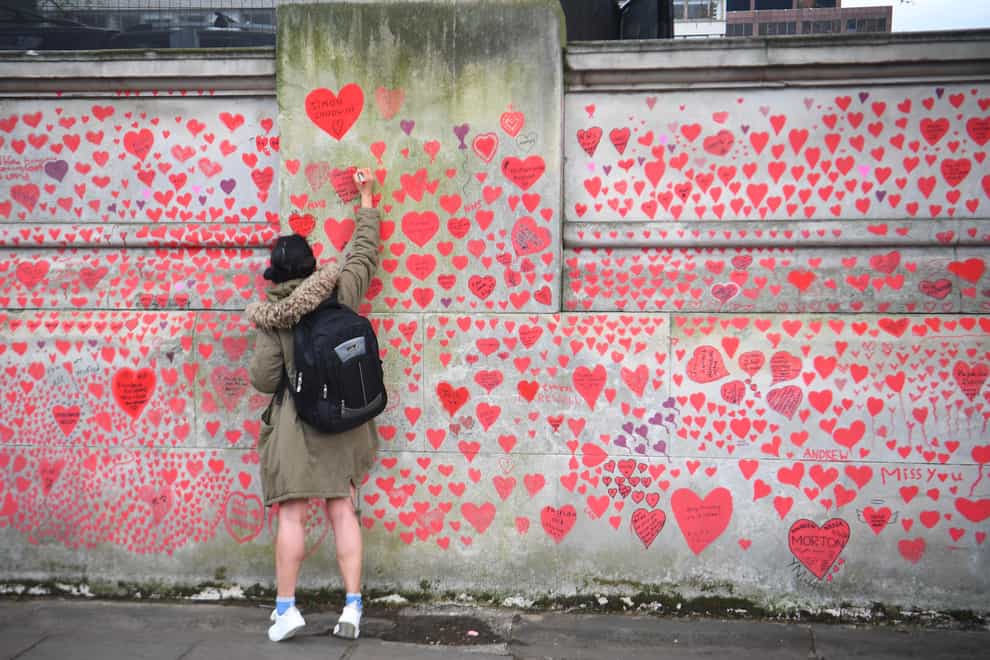A woman writes in a heart on the National Covid Memorial Wall on the Embankment in London (Victoria Jones/PA)