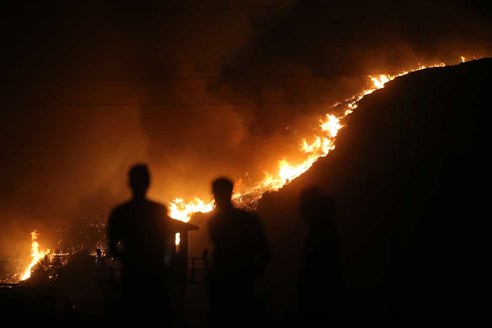 People stand in front of Kemerkoy thermal power plant with the blaze approaching in the background, in Milas, Mugla, Turkey (Emre Tazegul/AP)