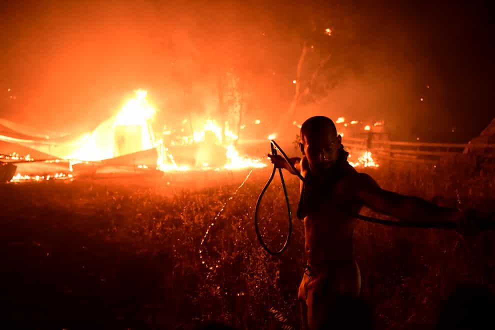 A man uses a water hose during a wildfire in Adames area, in northern Athens, Greece (Michael Varaklas/AP)