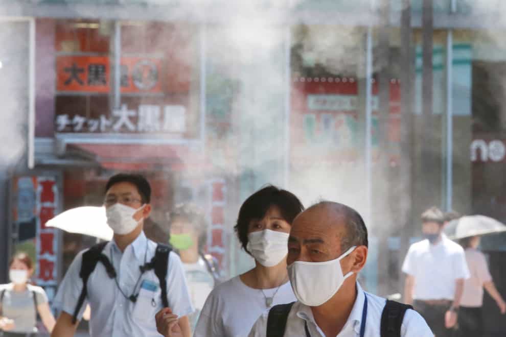 People wearing face masks to protect against the spread of the coronavirus walk under a water mist in Tokyo (AP)