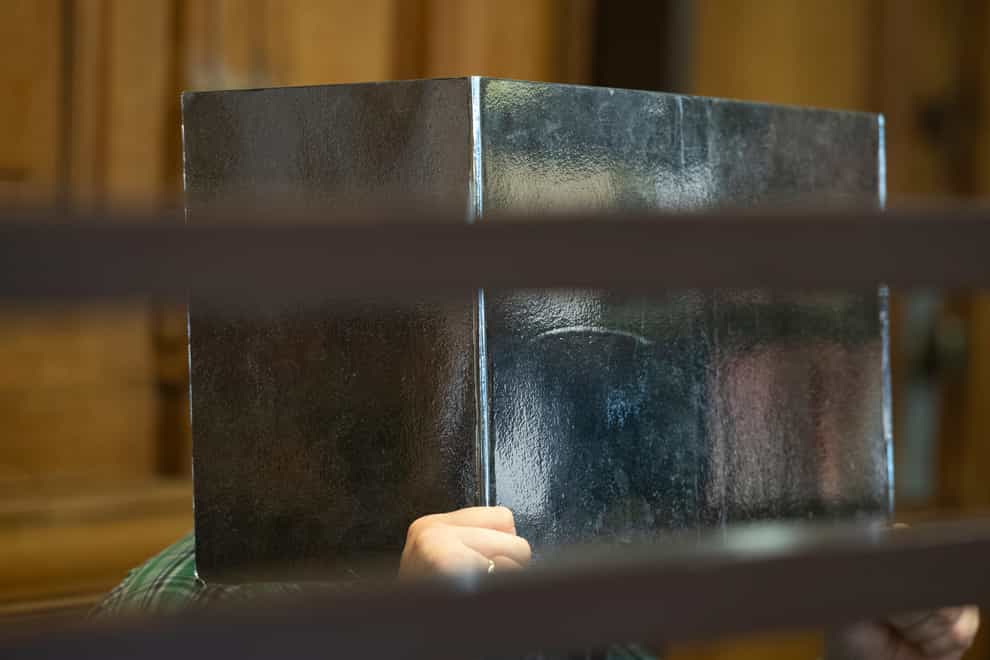 The defendant sits in a courtroom in Berlin, Germany, Tuesday, Aug. 10, 2021 holding a cardboard in front of his face. A German man who is suspected of having killed another man and eaten pieces of his body has gone on trial in Berlin. After the killing, which took place last September, the suspect allegedly chopped up the man’s body in his apartment on the northern outskirts of Berlin and then spread parts of it in different neighborhoods of the city, dpa reported from the trial’s beginning at a Berlin state court Tuesday. (Paul Zinken/dpa via AP)