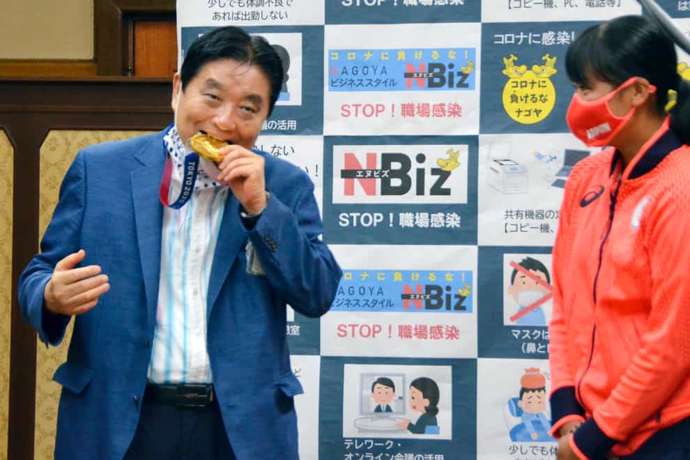 Nagoya mayor Takashi Kawamura, left, bites the Olympic gold medal of Miu Goto, right, of Japan softball team who won the event at the 2020 Summer Olympics (Kyodo News via AP)