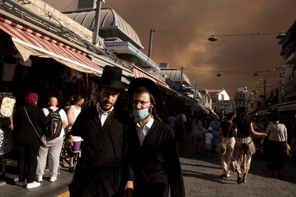 Ultra-Orthodox Jews stroll through the Machane Yehuda market under a sky darkened by nearby wildfires, in Jerusalem (Maya Alleruzzo/AP)