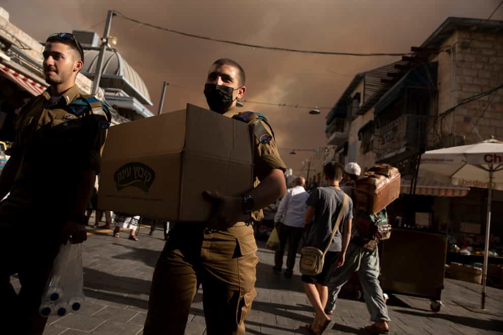 An Israeli soldier carries a box of sandwiches as he walks with a fellow soldier through the Machane Yehuda market under a sky darkened by nearby wildfires, in Jerusalem (Maya Alleruzzo/AP)