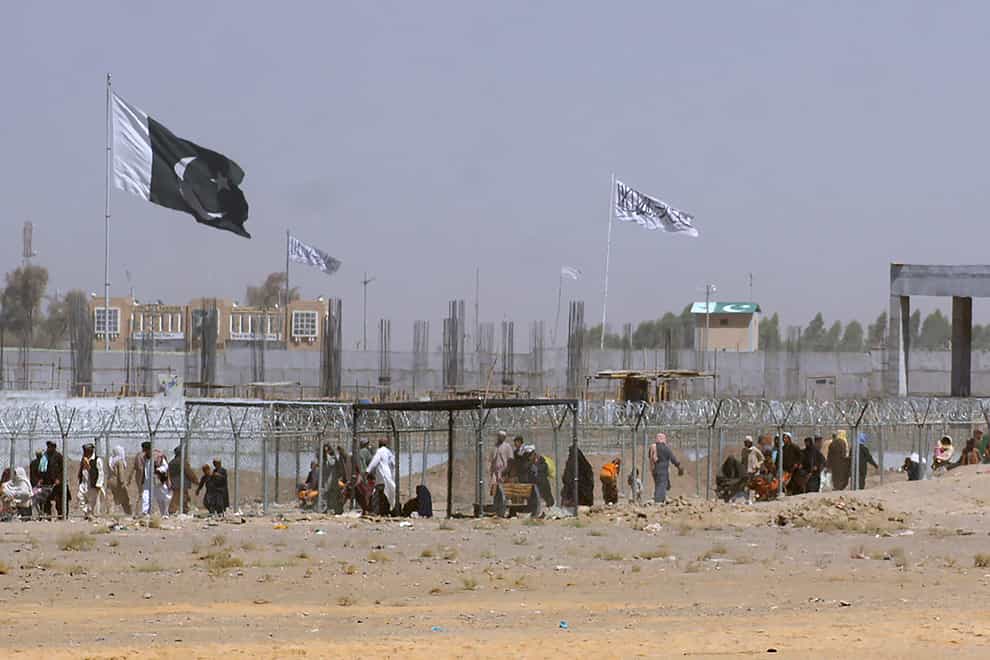 Pakistan and Taliban flags flutter on their respective sides while people walk through a security barrier to cross a border between Pakistan and Afghanistan, in Chaman, Pakistan (Jafar Khan/AP)