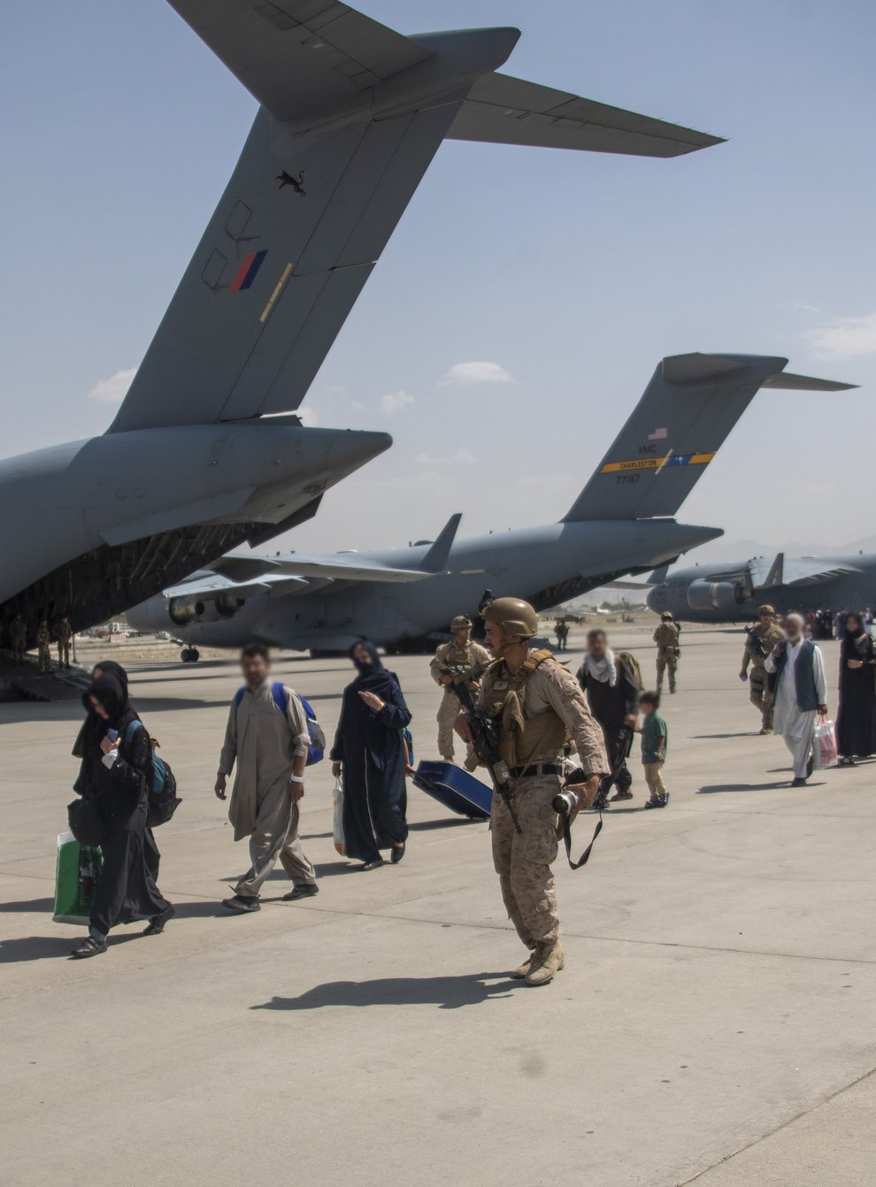 Members of the UK Armed Forces leading evacuees past a Royal Air Force Boeing C-17A Globemaster III at Kabul airport. (LPhot Ben Shread/MoD/PA)