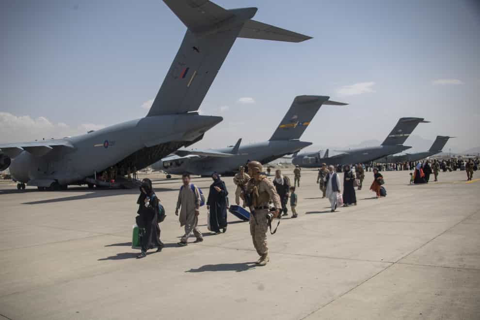 Members of the UK Armed Forces leading evacuees past a Royal Air Force Boeing C-17A Globemaster III at Kabul airport. (LPhot Ben Shread/MoD/PA)