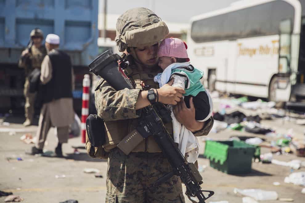 In this image provided by the U.S. Marine Corps, a Marine with the 24th Marine Expeditionary Unit (MEU) carries a baby as the family processes through the evacuation control center at Hamid Karzai International Airport in Kabul, Afghanistan, Saturday, Aug. 28, 2021. (Staff Sgt. Victor Mancilla/U.S. Marine Corps via AP)