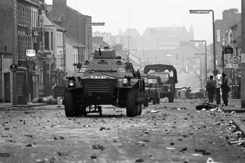 Armoured cars rumble over the rubble past overturned cars and a wrecked motor cycle at dawn in Belfast’s Protestant Shankill Road, after a night of violence in which three people died.