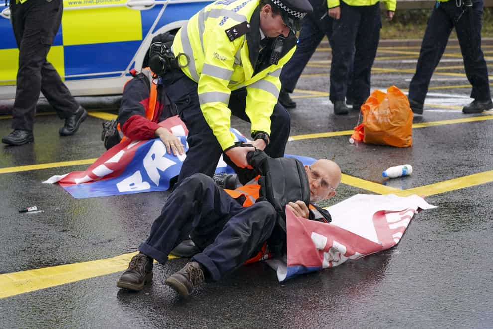 Police officers detain a protester from Insulate Britain occupying a roundabout leading from the M25 motorway to Heathrow Airport in London.(Steve Parsons/PA)