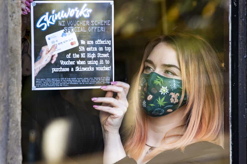 Tattoo apprentice Amy Lawless posts an ad in the window of Belfast City Skinworks, Tattoo and Piercing Studio. The studio is offering 50% extra on top of the Northern Ireland High Street voucher scheme, when using it to purchase a Skinworks voucher (Liam McBurney/PA)
