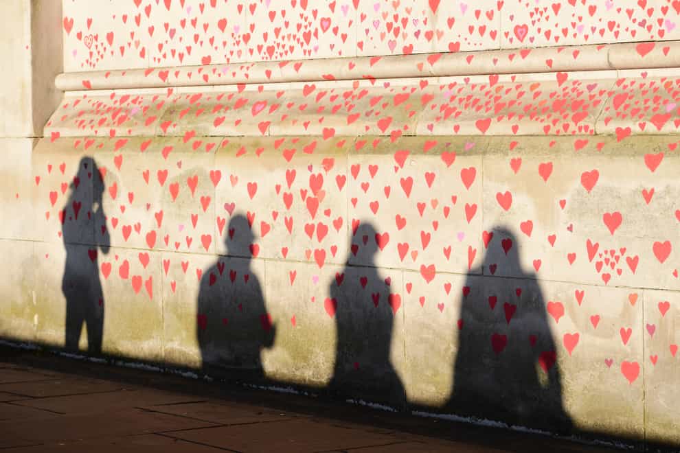 People are silhouetted against the Covid-19 Memorial Wall on the Embankment, central London (Ian West/PA)