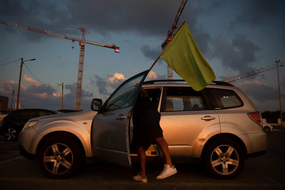 A man places a green flag on his car as he prepares to join a convoy of cars and protest against the green pass changes (Oded Balilty/AP)