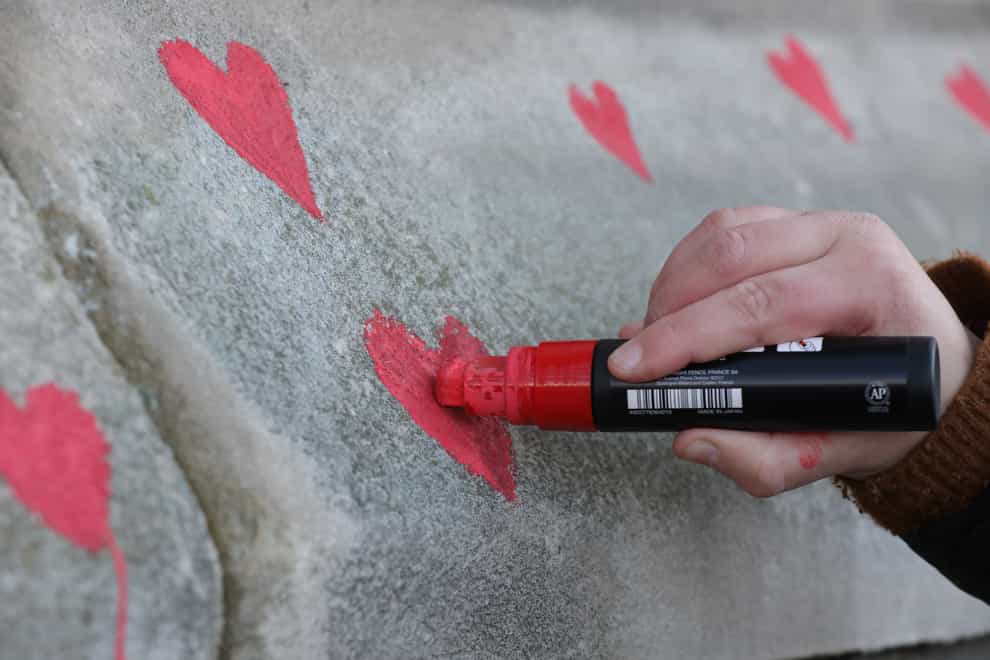 Members of bereaved families paint red hearts on the Covid-19 Memorial Wall opposite the Houses of Parliament (Lucianna Guerra/PA)