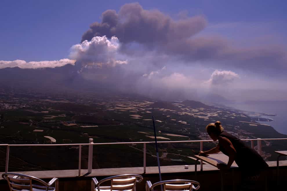 A worker cleans the ash from the tables of a restaurant as lava flows from a volcano on the Canary island of La Palma, Spain on Monday Oct. 4, 2021. More earthquakes are rattling the Spanish island of La Palma, as the lava flow from an erupting volcano surged after part of the crater collapsed. Officials say they don’t expect to evacuate any more people from the area, because the fiery molten rock was following the same route to the sea as earlier flows. (AP Photo/Daniel Roca)