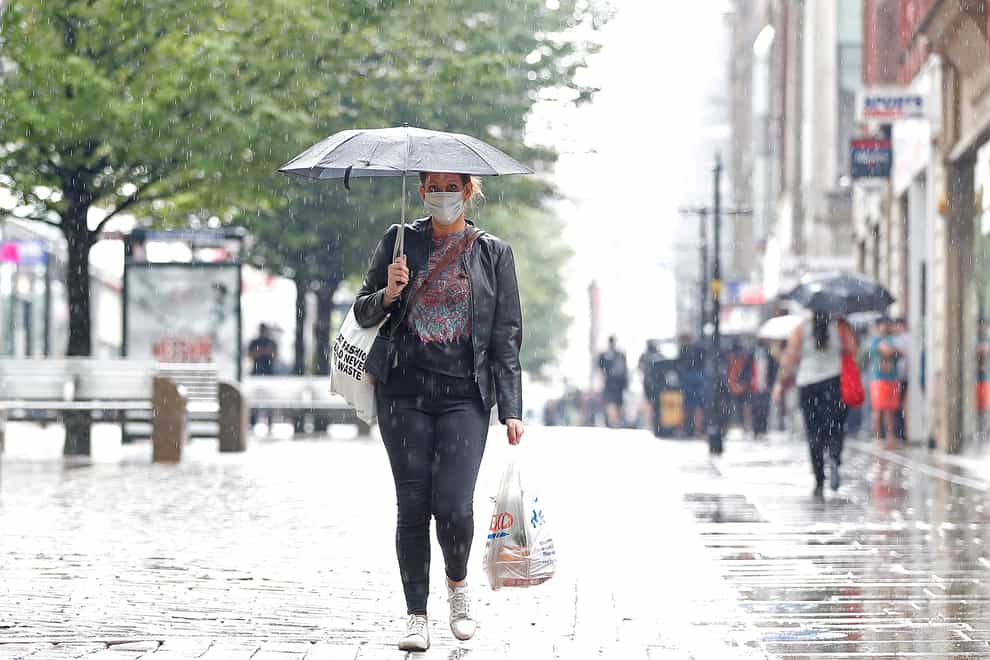 A shopper shelters from the rain on Market Street in Manchester (Martin Rickett/PA)