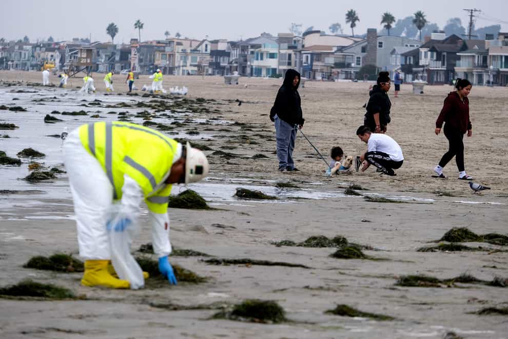 Workers in protective suits clean the contaminated beach after an oil spill in Newport Beach, California (AP)