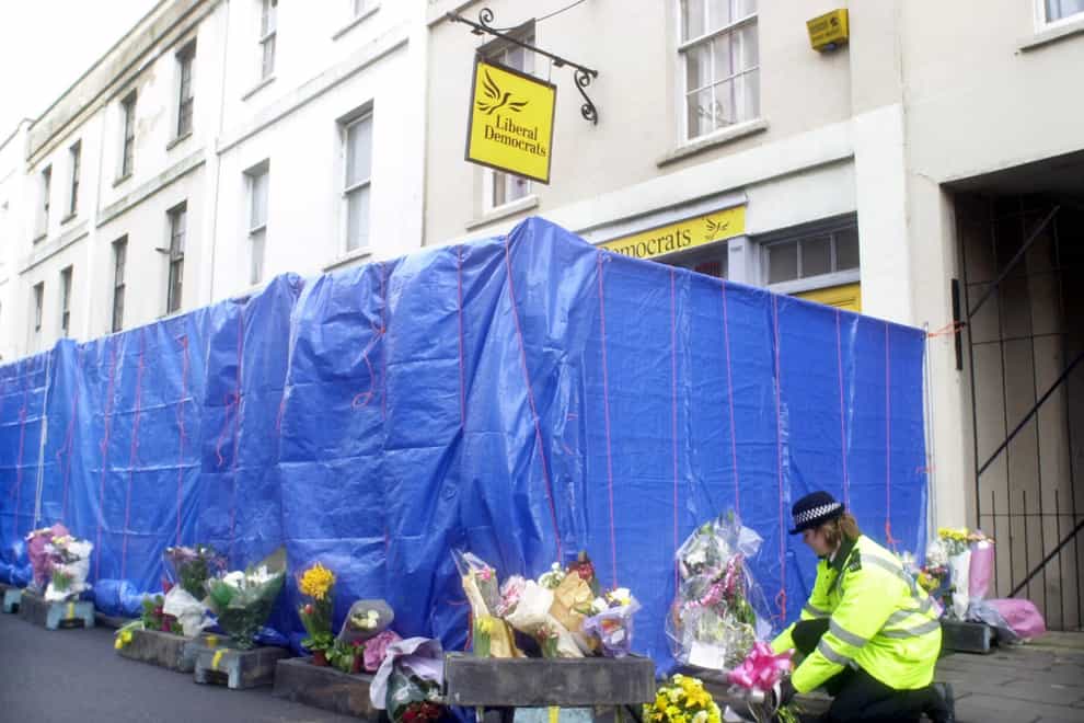 A police officer with floral tributes left outside the Cheltenham offices of the Liberal Democrats (Barry Batchelor/PA)