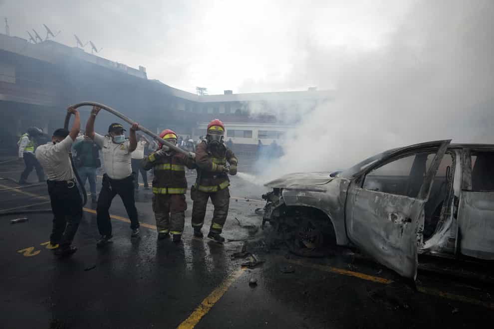 Firefighters and police work together to douse a vehicle with water (Moises Castillo/AP)
