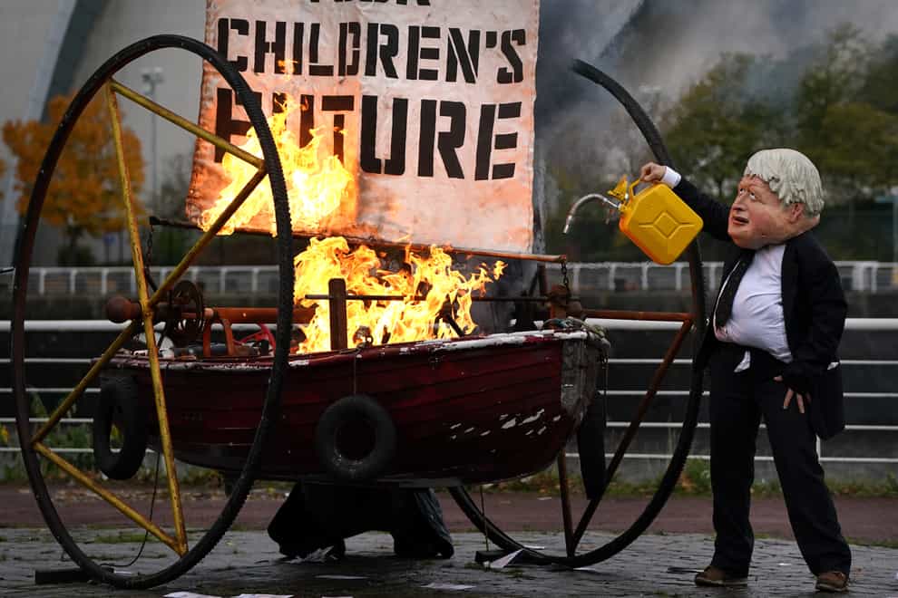 An Ocean Rebellion protester dressed as Prime Minister Boris Johnson sets fire to the boat sail (Andrew Milligan/PA)