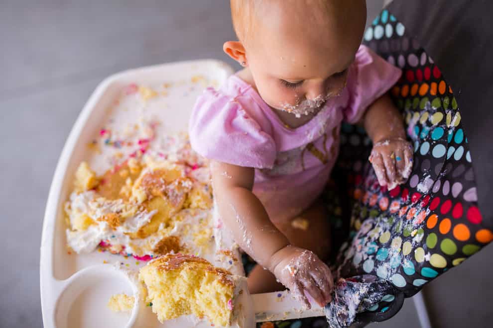 Baby girl happily playing with food (Alamy/PA)