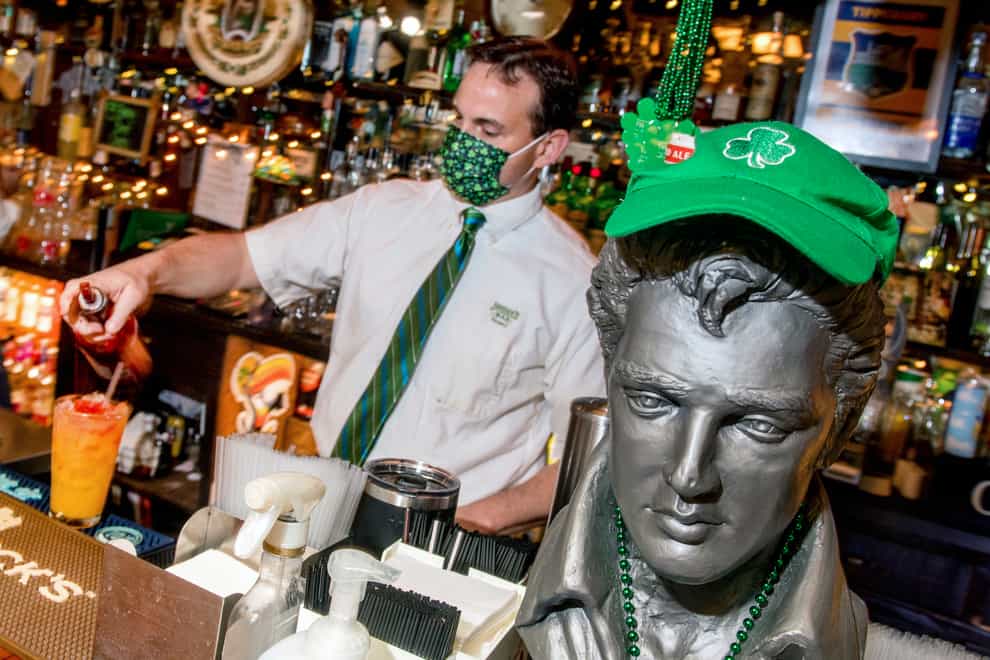 A bust of Elvis Presley wearing a shamrock cap and beads stands guard as bartender Tom Eckstein mixes a drink for St Patrick’s Day. The bust was stolen but is now back (Matt Dayhoff/Journal Star via AP)