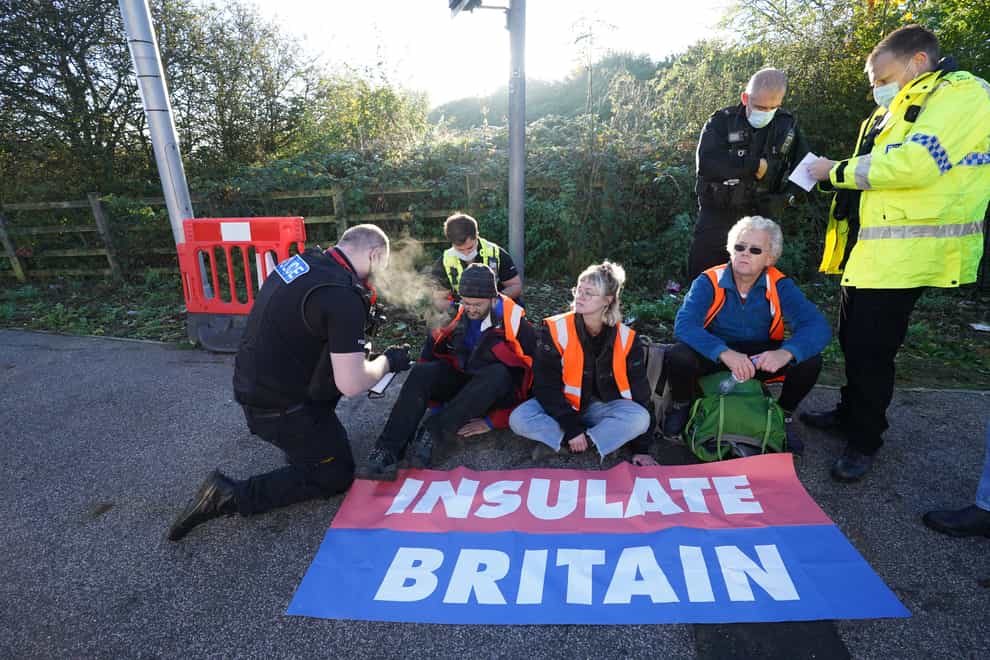 Police officers speak to protesters at an Insulate Britain roadblock near to the the South Mimms roundabout at the junction of the M25 and A1. (Ian West/PA)