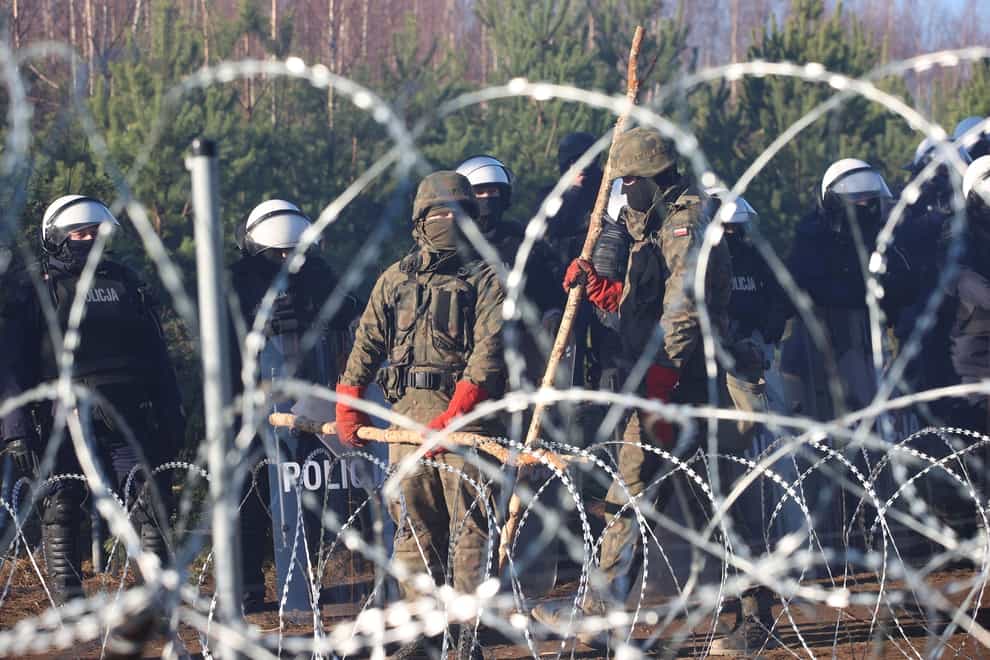 FILE – Polish police and border guards stand near the barbed wire as migrants from the Middle East and elsewhere gather at the Belarus-Poland border near Grodno Grodno, Belarus, Tuesday, Nov. 9, 2021. Thousands of migrants flocked to Belarus’ border with Poland hoping to get to Western Europe, an influx that prompted Polish authorities to introduce a state of emergency and deploy thousands of troops and police. (Leonid Shcheglov/BelTA via AP, File)
