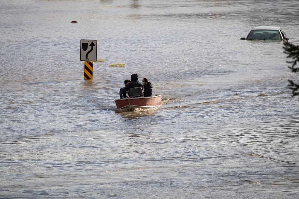 People who were stranded by high water due to flooding are rescued by a volunteer operating a boat in Abbotsford, British Columbia (Darryl Dyck/The Canadian Press via AP)