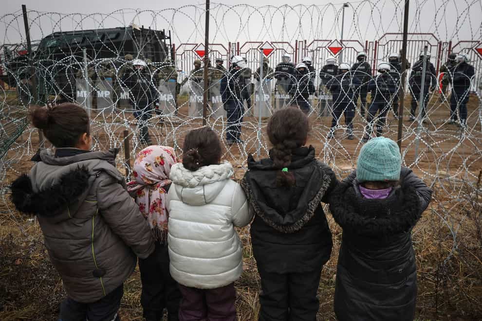 Migrant children in front of a barbed-wire fence and Polish servicemen on the Belarus/Poland border near Grodno in Belarus (Maxim Guchek/BelTA via AP)