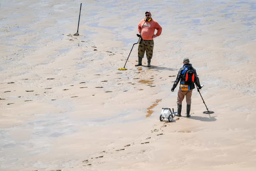 People with metal detectors stop and chat to each other while scouring the beach in Woolacombe, Devon (PA)