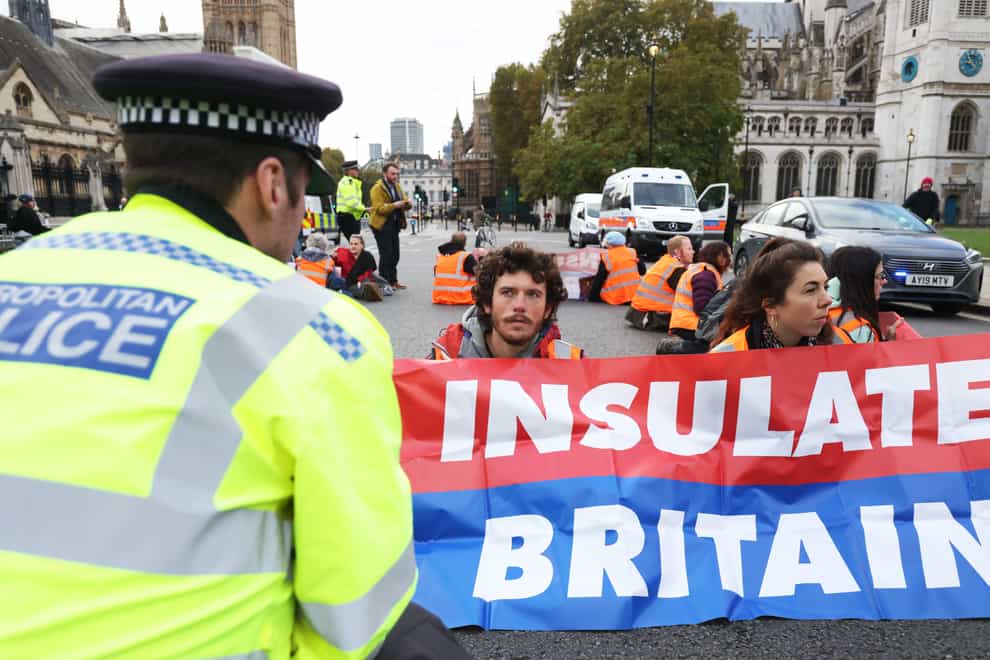 A police officer speaks to protesters from Insulate Britain as they block the road in Parliament Square, central London, earlier this month (PA)