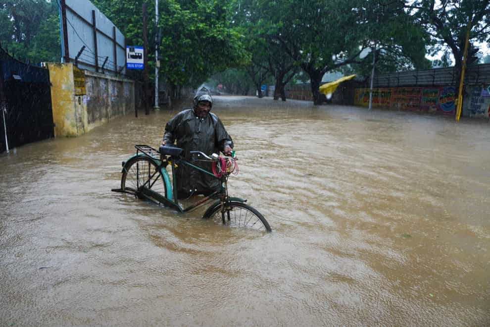 A man pushes his bike through a flooded street in Chennai, in the southern Indian state of Tamil Nadu (R Parthibhan/AP)