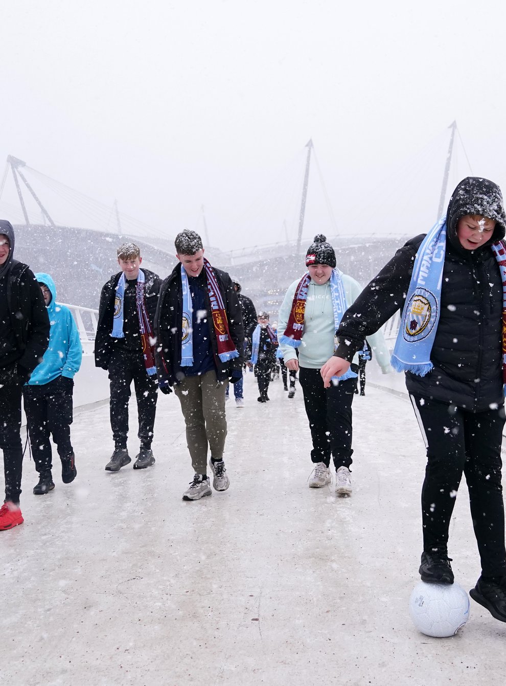 Fans cross the bridge to the Etihad Stadium in the snow before Manchester City’s game with West Ham (Martin Rickett/PA)