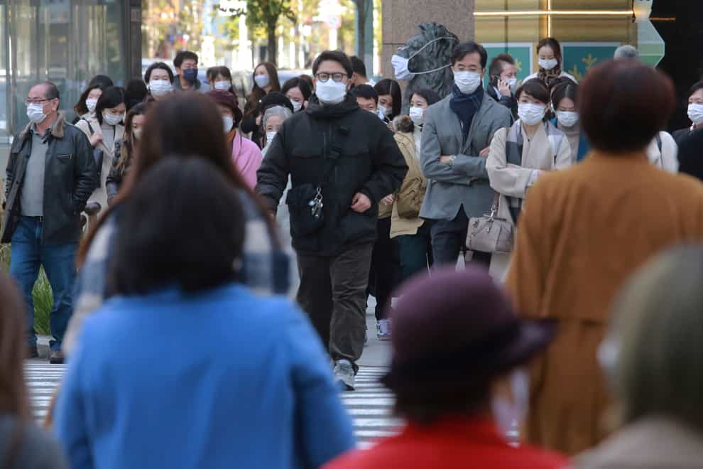 People wearing face masks to protect against the spread of coronavirus walk along a street in Tokyo (Koji Sasahara/AP)